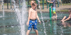 A little kid in a blue swim suit gets sprayed with water in a splash park.