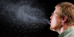 A man sneezes on a black background so you can see all the spit droplets.