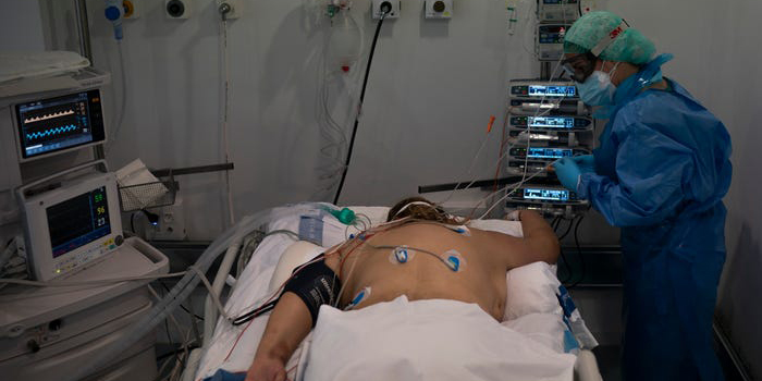 A nurse checks on man on his belly in a hospital bed. He is hooked up to a ventilator.