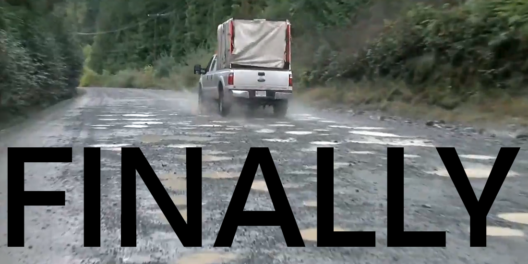 A truck drives away along a pockmarked logging road in the rain.