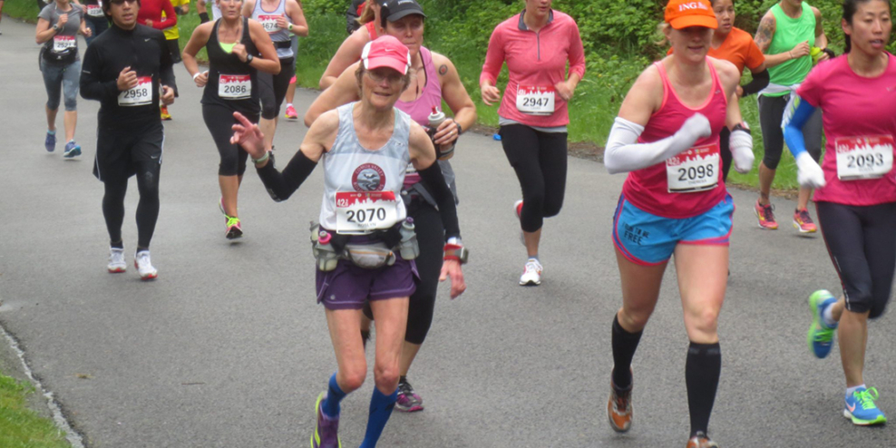 Roslyn Smith waves to the camera in a pack of brightly dressed runners.