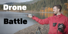 A man in a red jacket carrying a giant camera holds a drone up so the pilot can launch it from his hand.