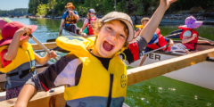 A group of youngsters paddle a giant canoe. They look very excited, and it's a sunny day.