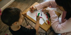 A little kid sits at a small table with an early childhood educator and they practice drawing together.