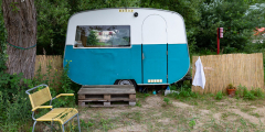 A little camper sits on palettes. The bottom is blue and the top is white. It's not attached to a vehicle.