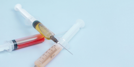 Three syringes full of liquid sit on a pale blue table.