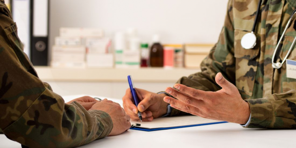 A closeup of two military officials hands sitting across from each other at a desk; one of them has a stethoscope around his neck.